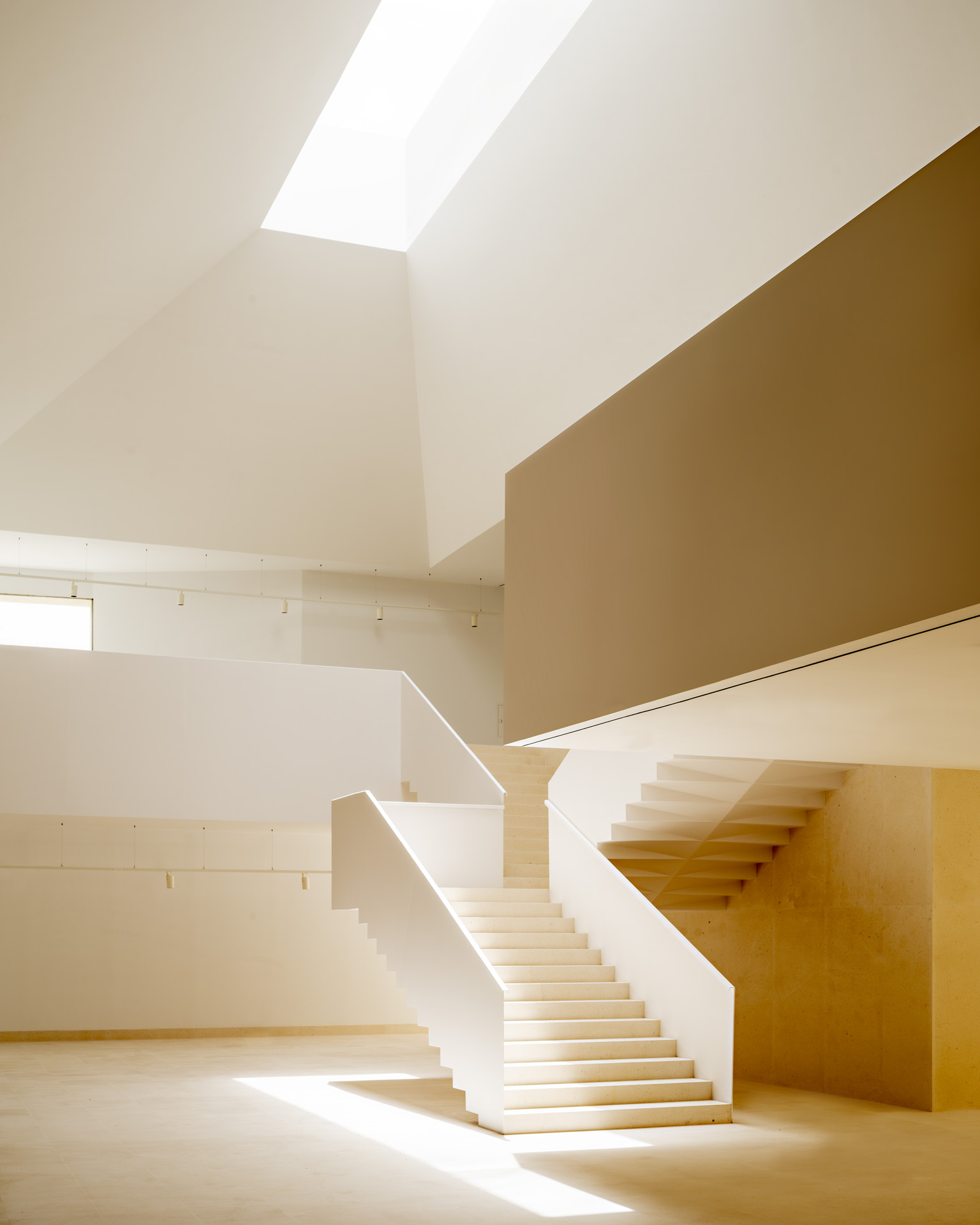 White staircase rising through a sunlit void