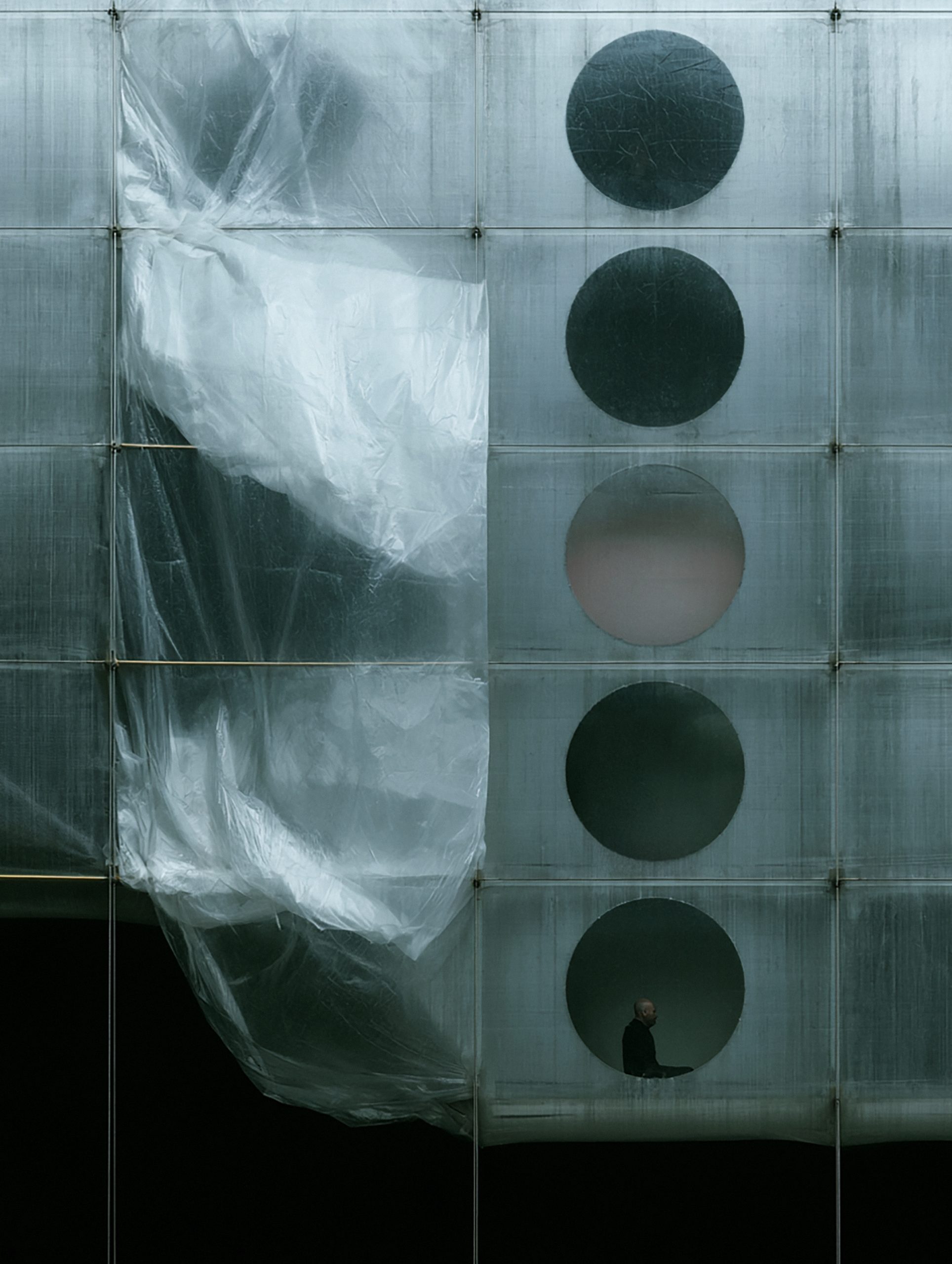 Translucent modular facade with circular openings and a small seated figure in MóDULO De ViDA