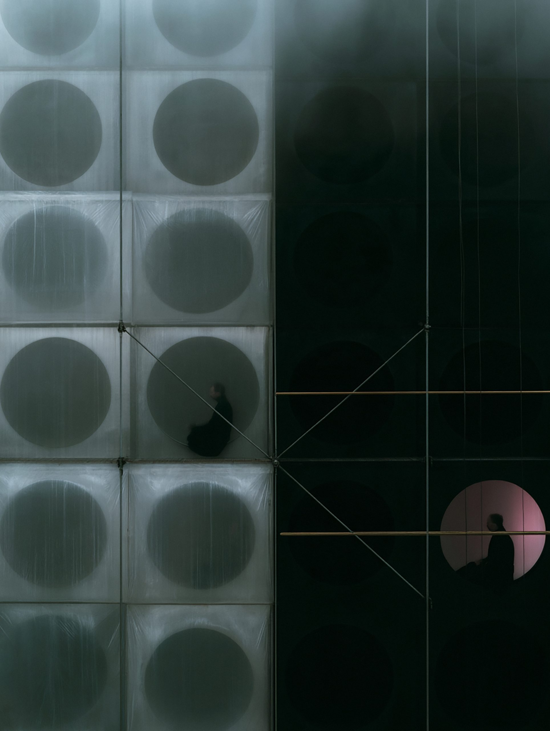 Dark modular grid with circular openings and a silhouetted inhabitant by DOISDOIS