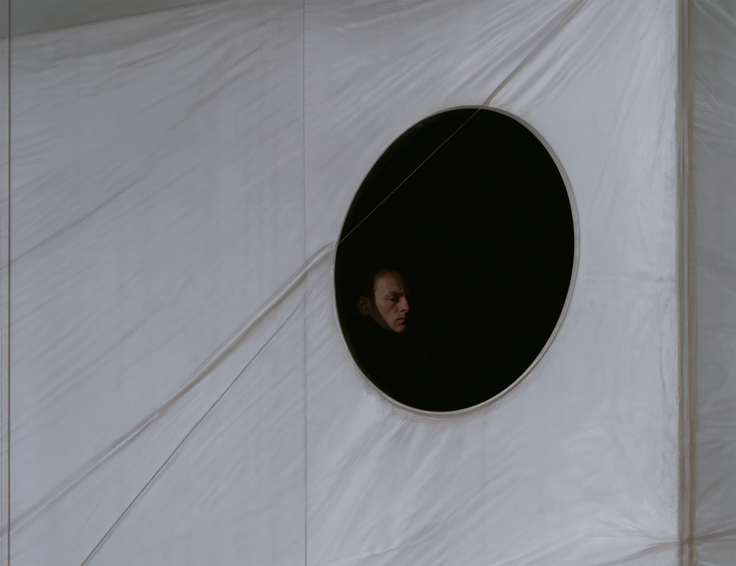 An inhabitant looks out through a circular opening in a white membrane