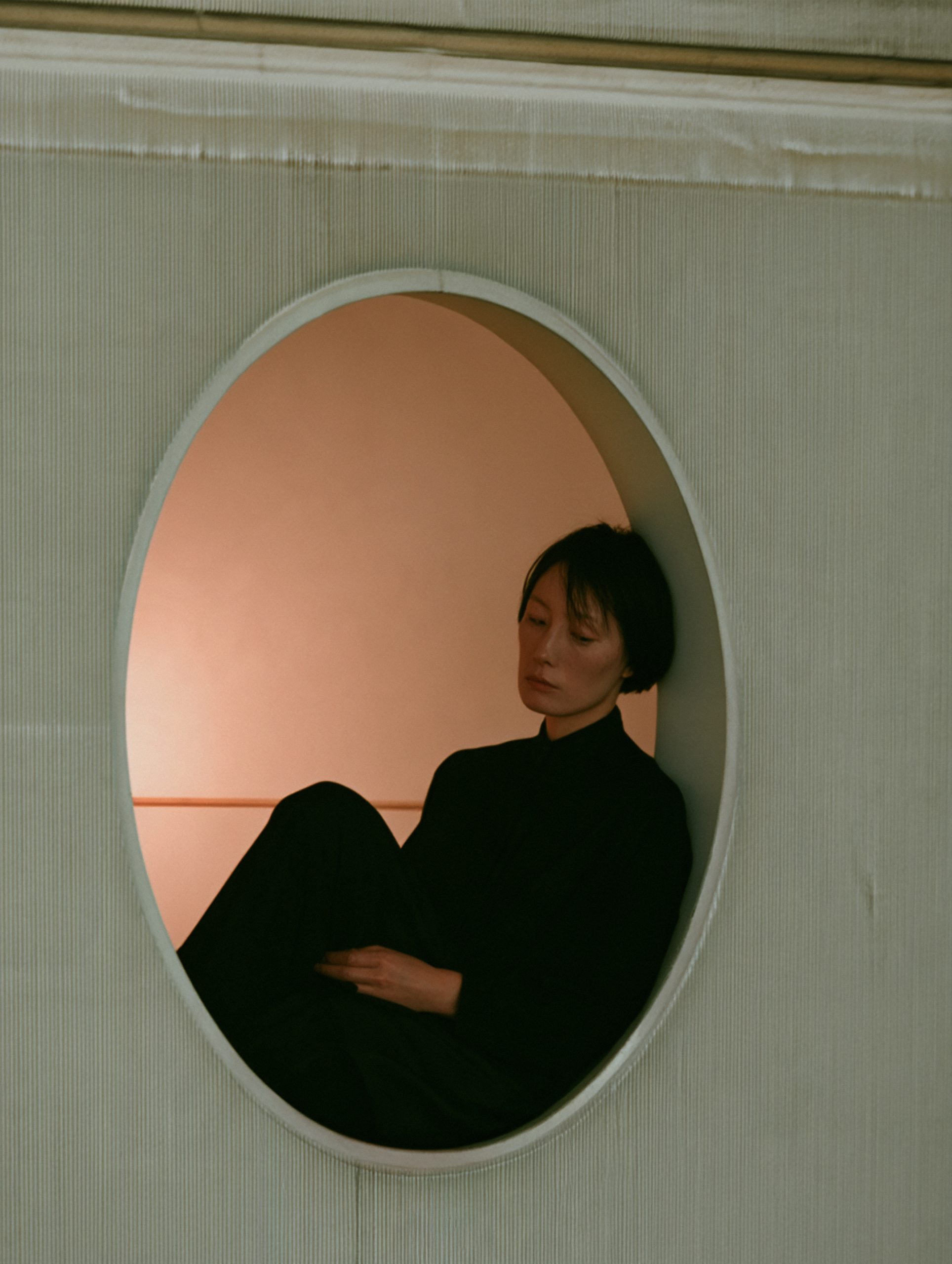 A seated woman framed by a circular opening with a softly lit interior