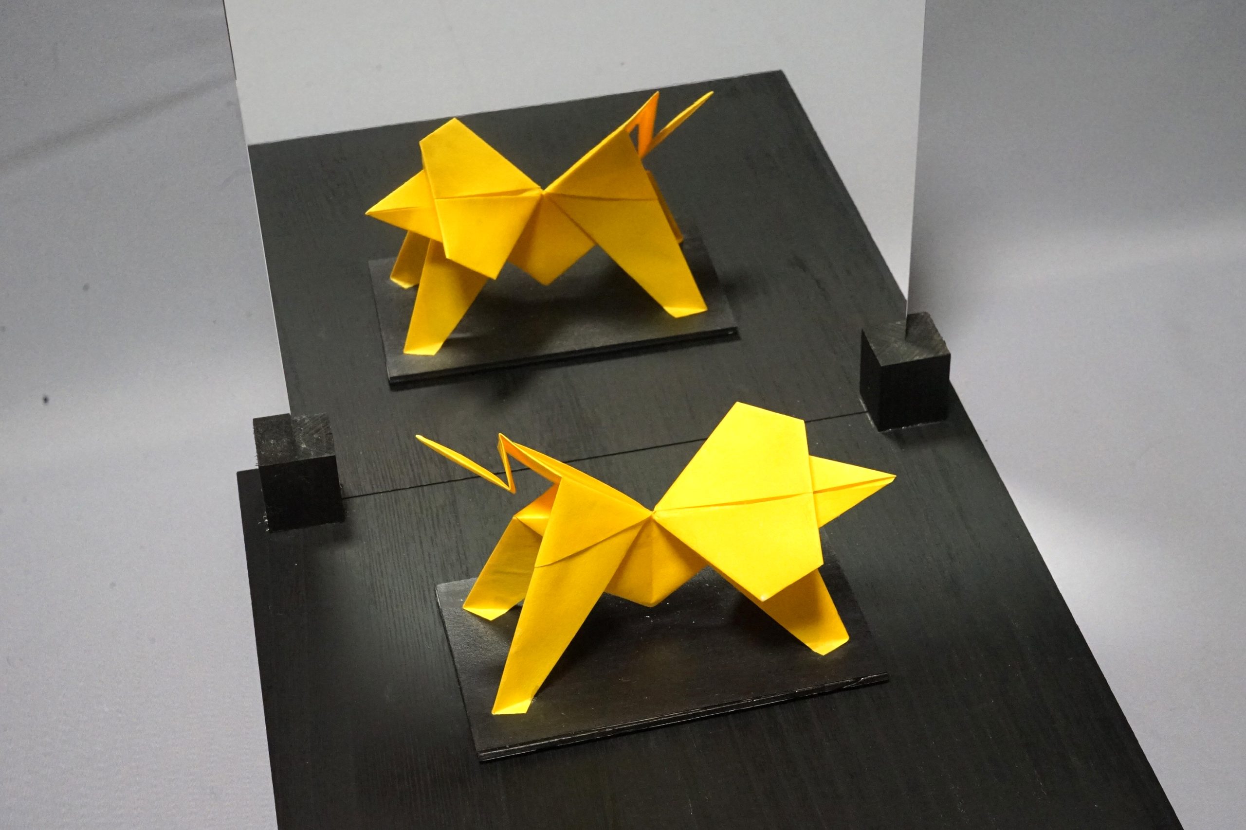 Yellow origami lions beside a mirror, Lions Passing Each Other, 2025, by Kokichi Sugihara