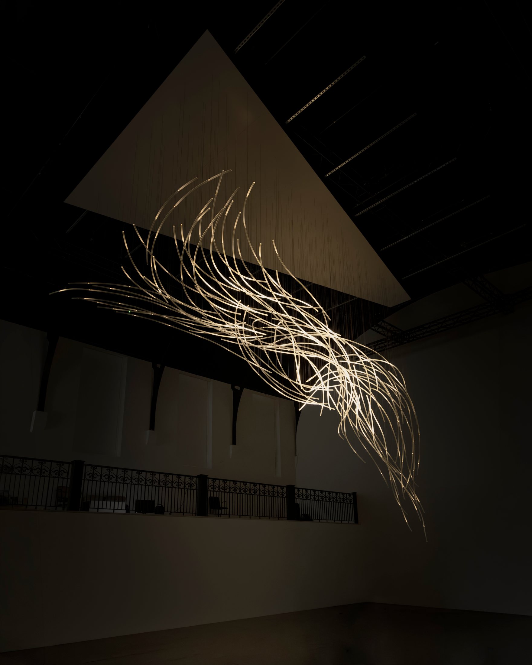 Illuminated glass strands of Aeolus beneath its overhead support