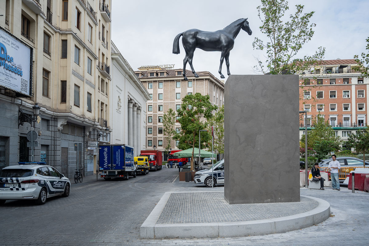 Wide view of the bronze horse sculpture with surrounding streets, buildings and trees