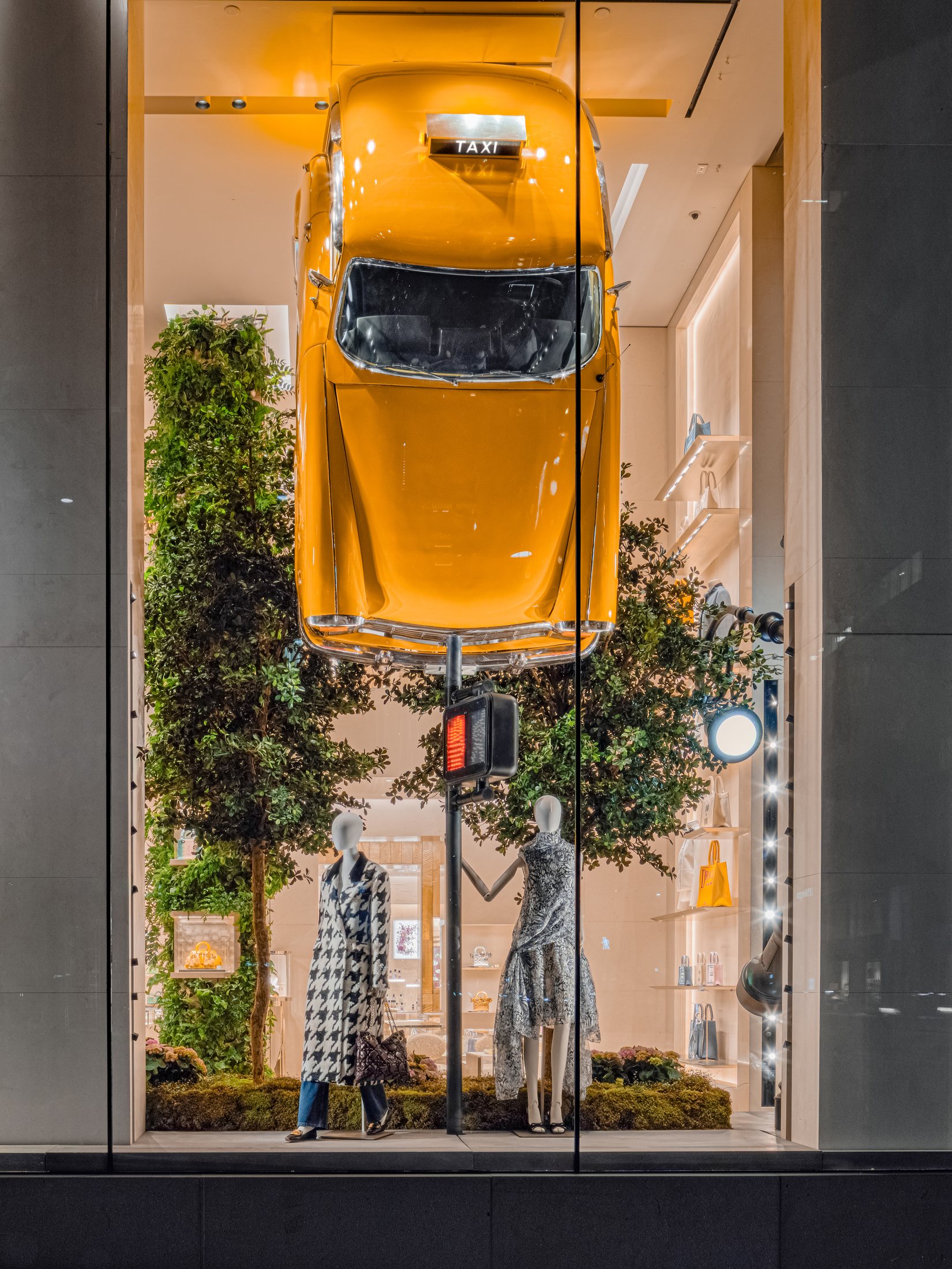 Yellow taxi suspended vertically above planting in the New York Dior window