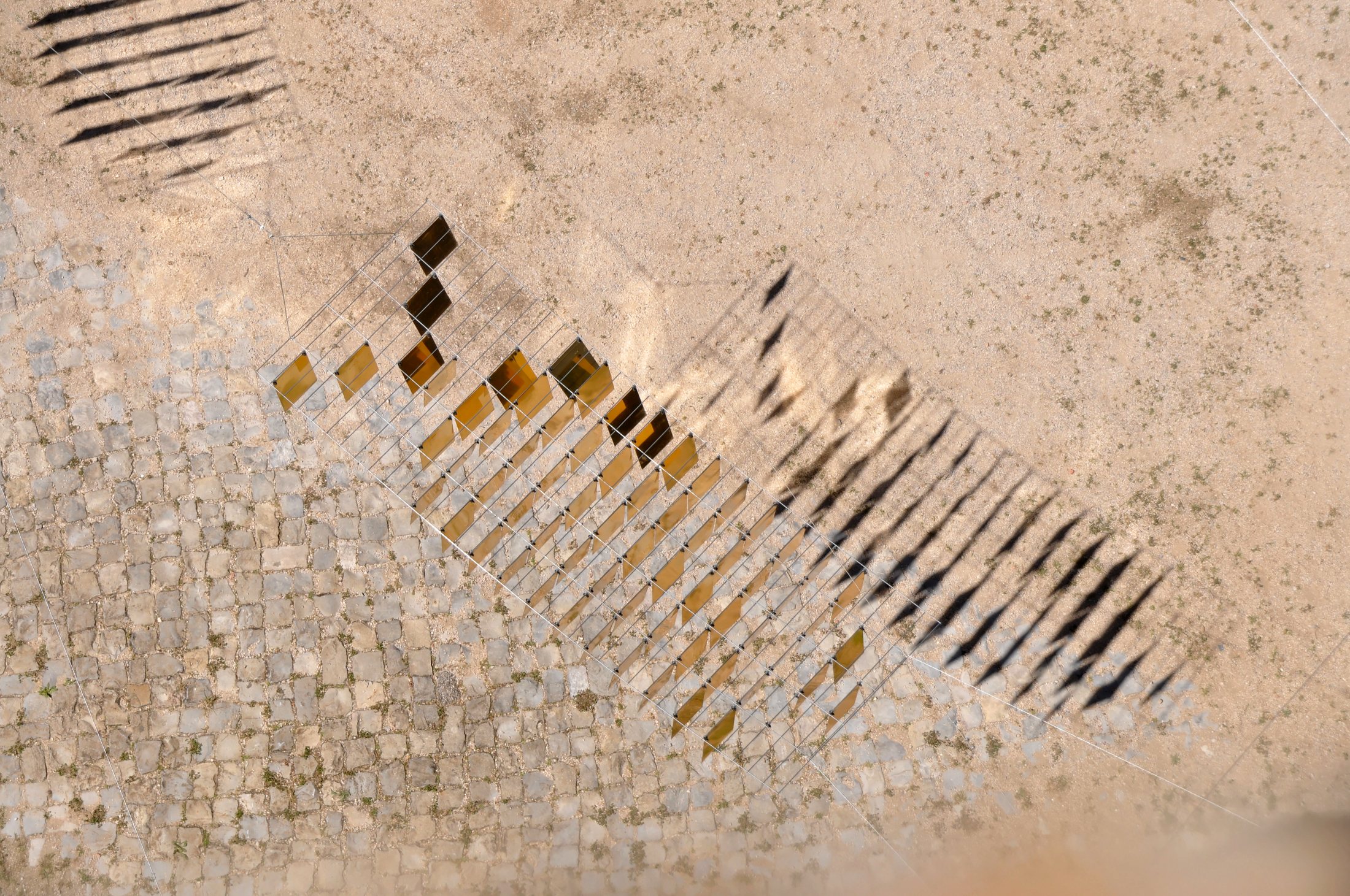 Rectangular reflections and narrow shadows cast onto the courtyard paving