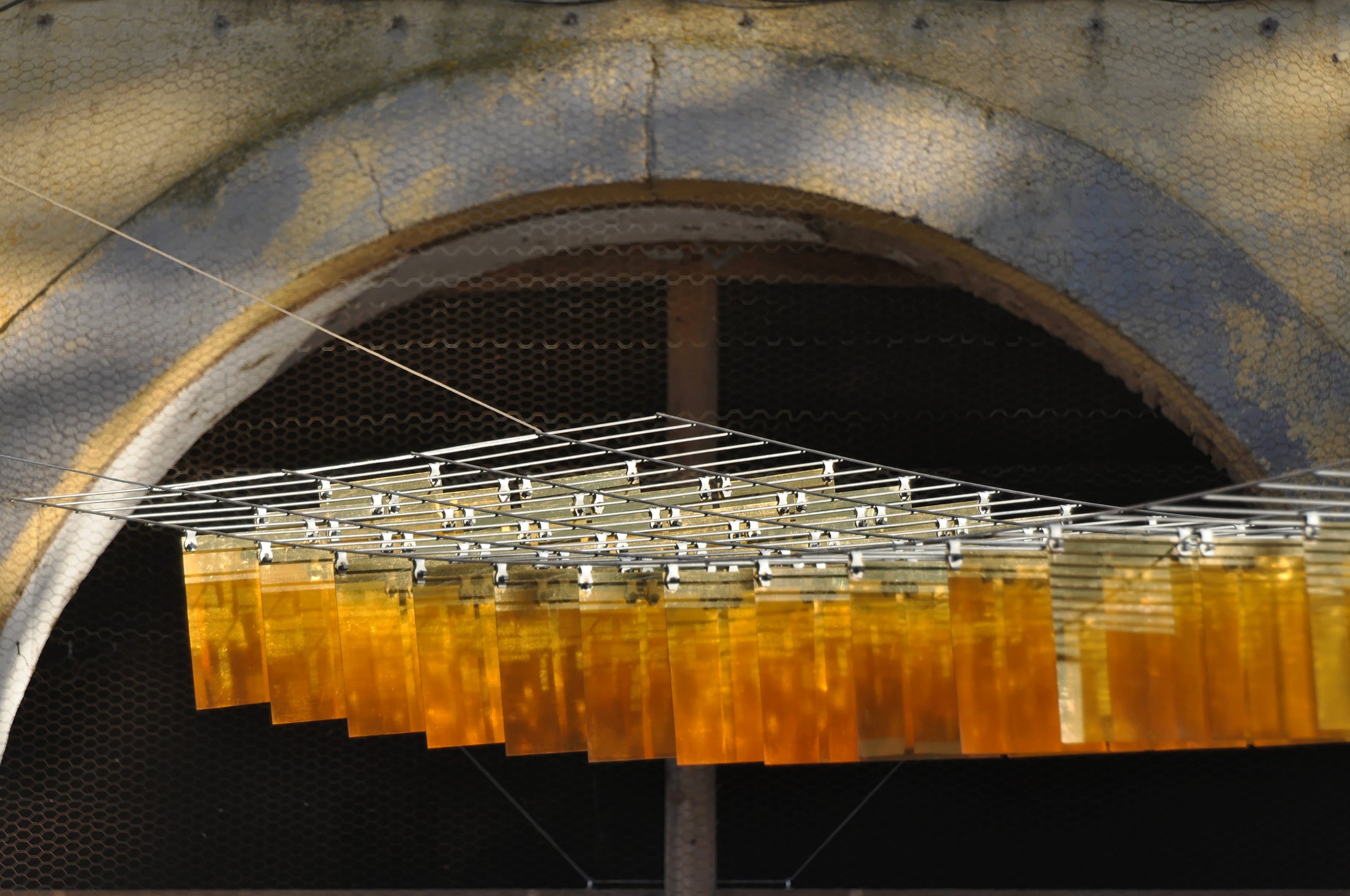 Golden panels and crossing suspension wires in front of a stone arch