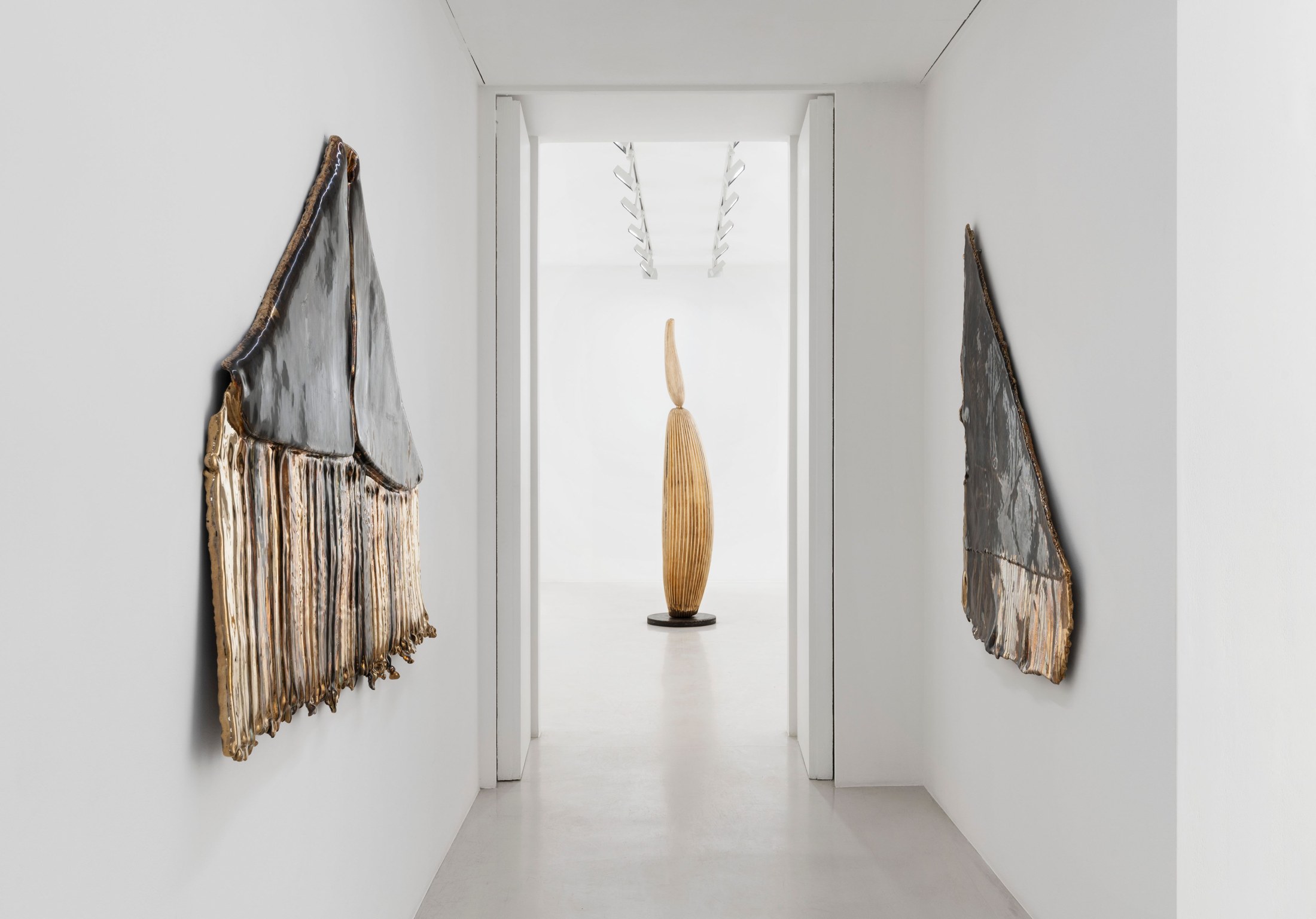 Folded bronze wall reliefs flanking a doorway with an upright sculpture beyond