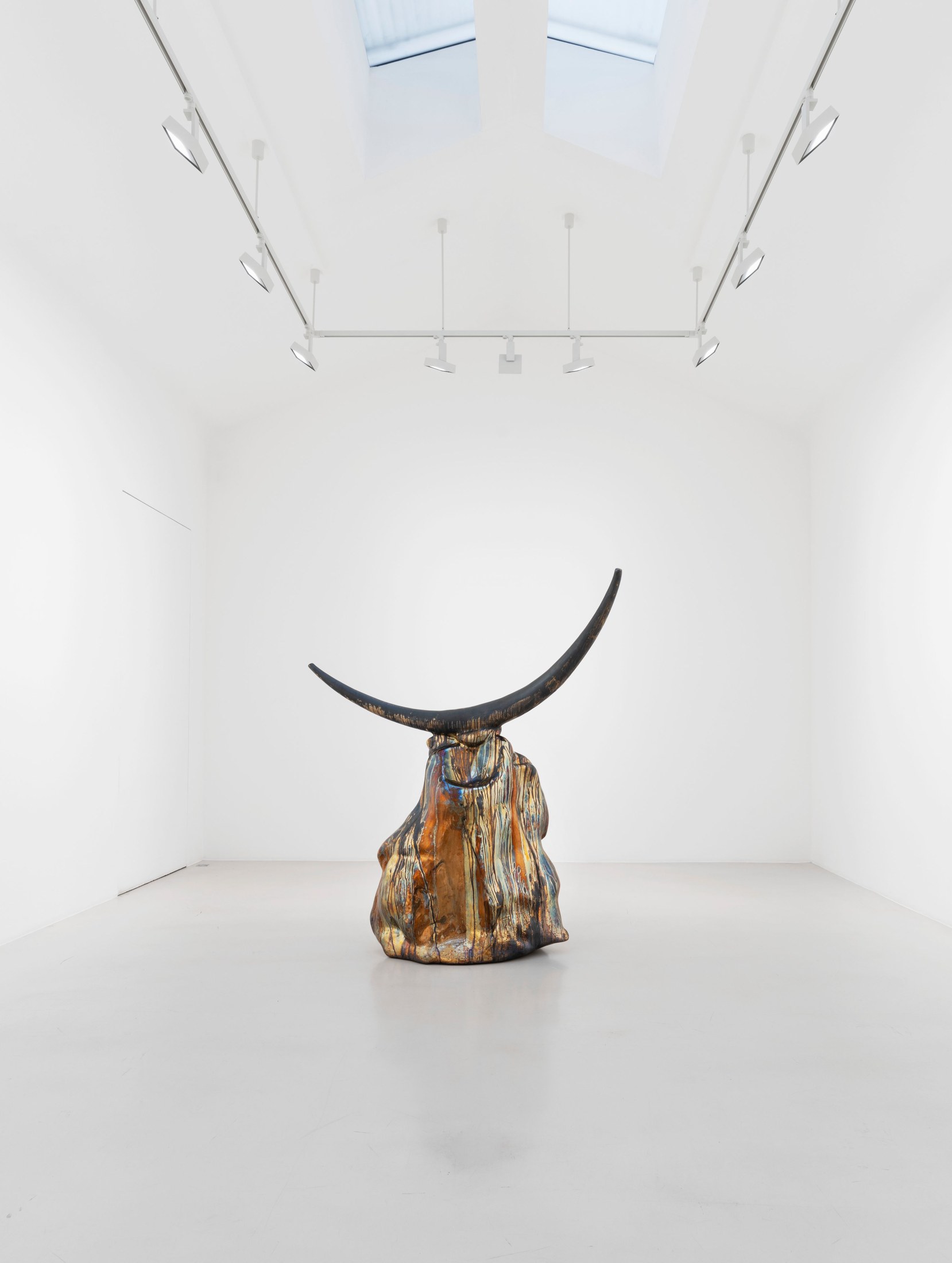 Dark crescent-shaped element above a polished bronze base in Alma Allen’s exhibition