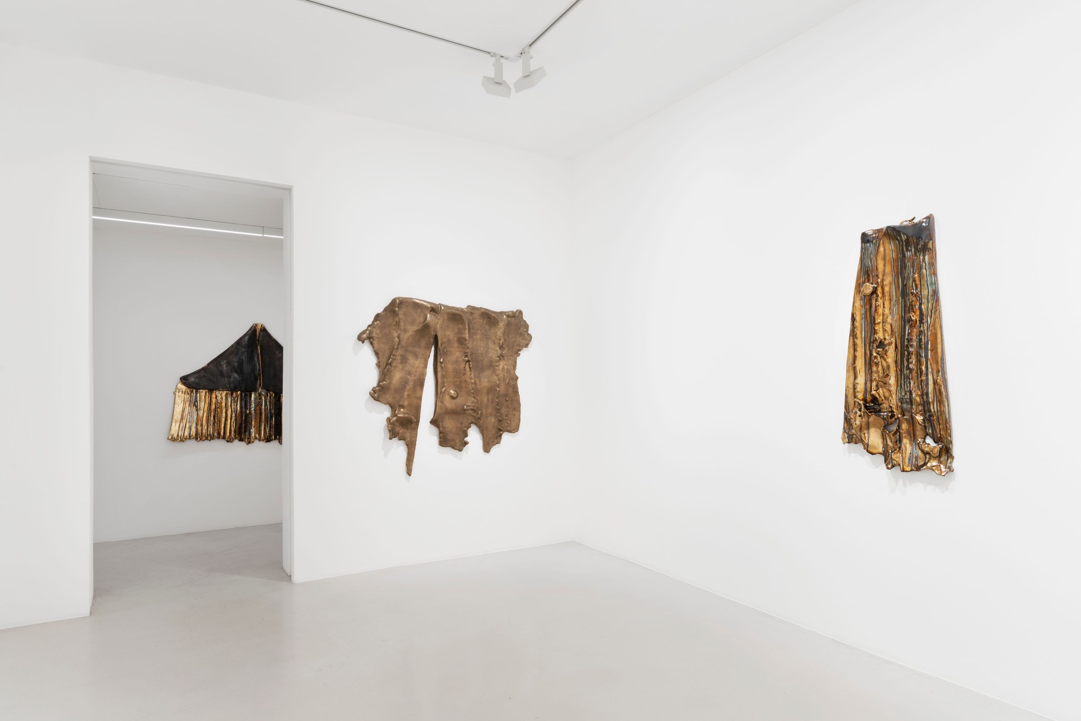Wall reliefs and an upright pleated sculpture across adjoining exhibition rooms