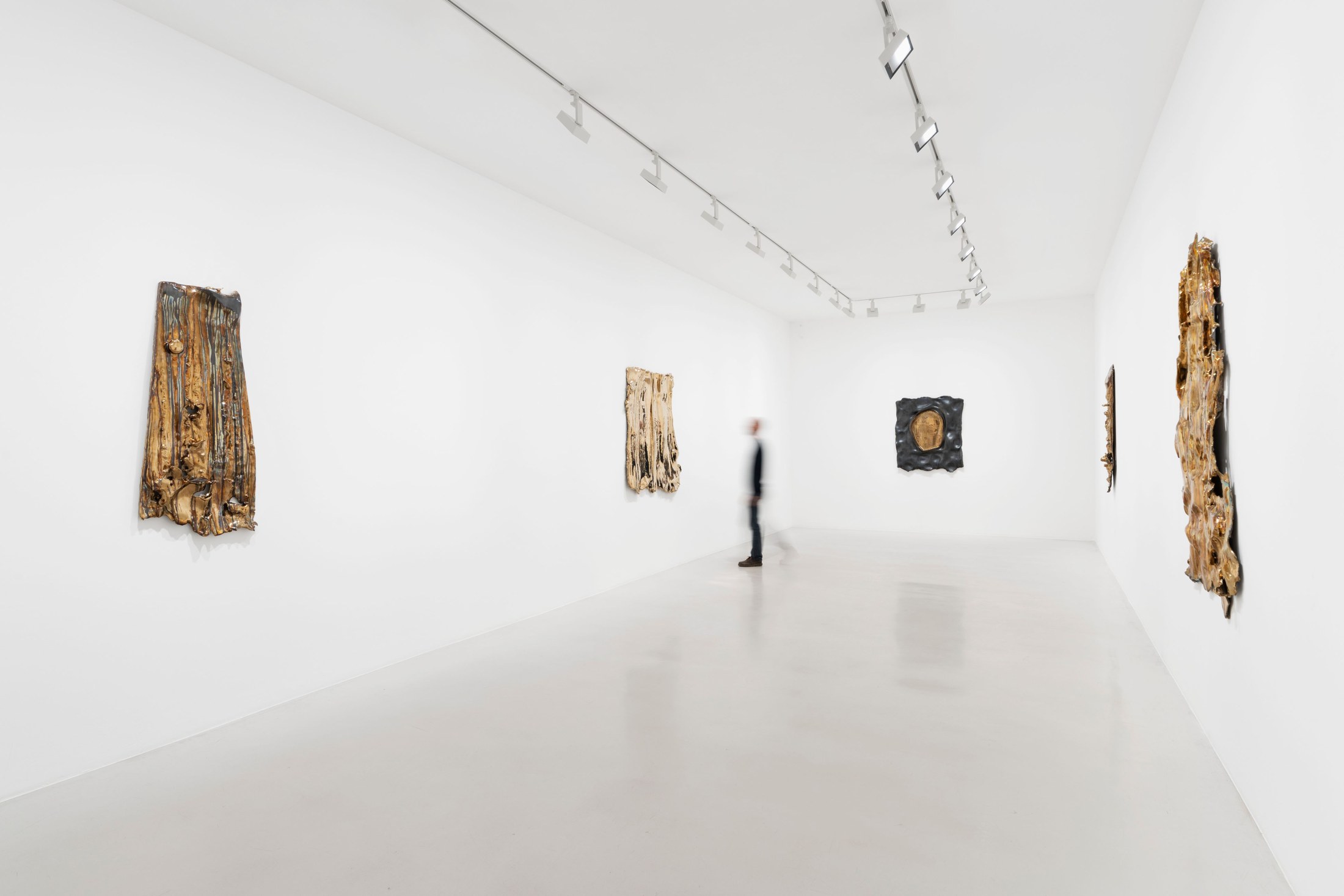 Visitor facing bronze wall reliefs in the bright Perrotin gallery
