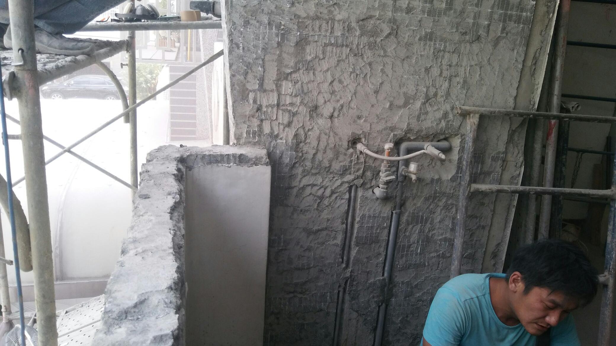 1) 照片顯示一個正在施工的建築物，有水泥牆和鋼筋，有一個穿著藍色上衣的工人在牆邊工作