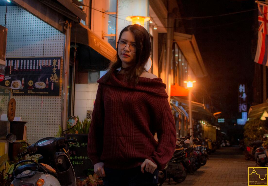 這張「在街邊夜市」的照片是一個年輕女子,她穿著紅色毛衣,站在街邊,背後是昏暗的街景。