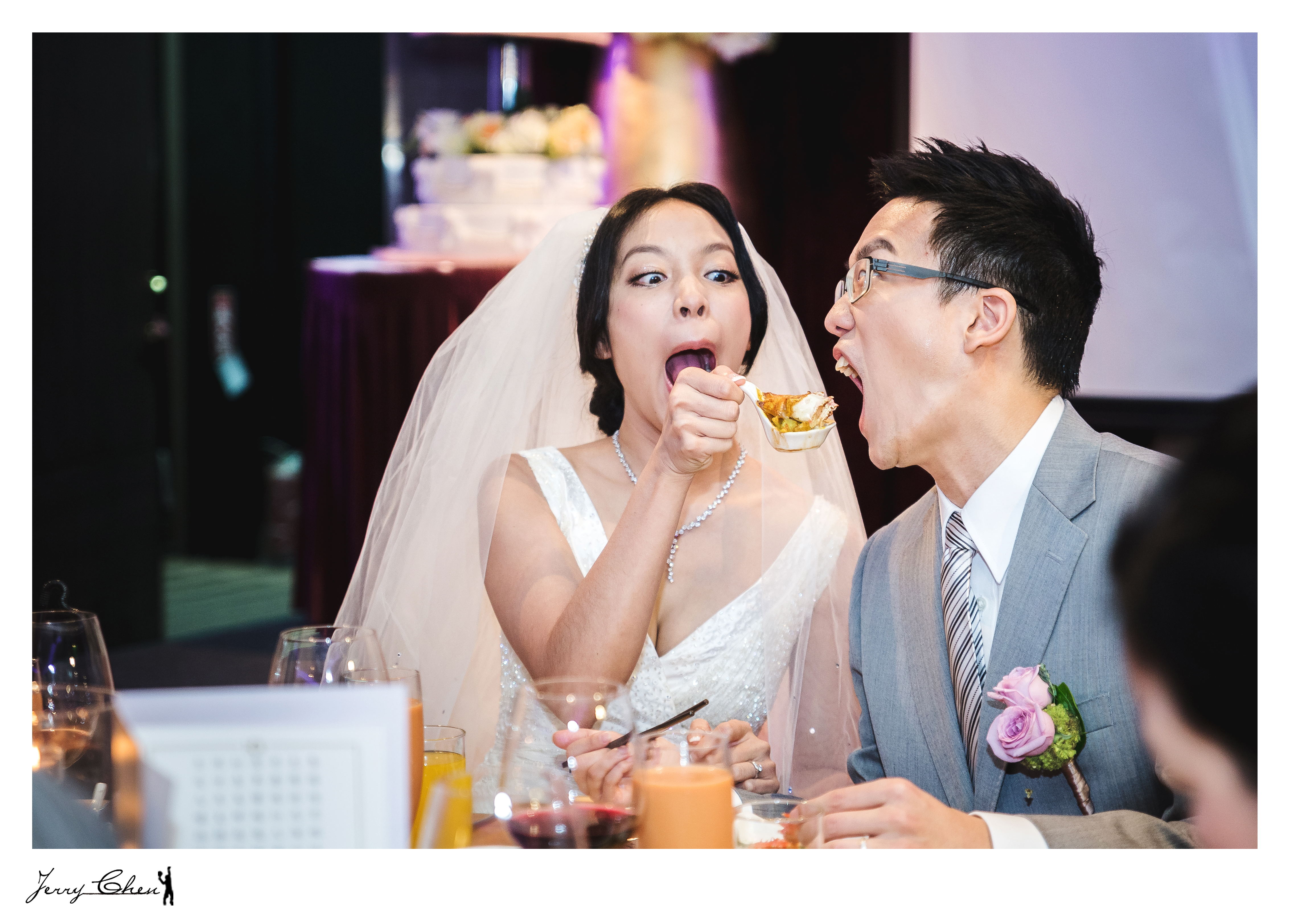 這張照片是一對新人在婚禮宴會上吃東西。新娘穿著白色婚紗,新郎穿著灰色西裝。新娘正用叉子吃著一塊食物,新郎則在看著她。他們的表情都非常自然,充滿了幸福感。