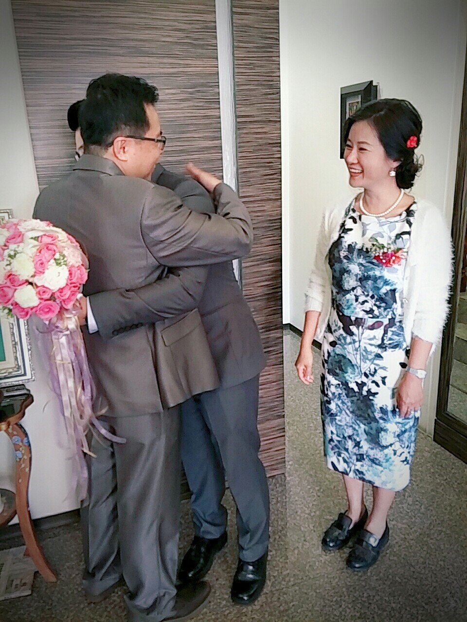 這張「婚禮」的照片是兩位穿著西裝的男士和一位穿著禮服的女士。女士手拿著花束,而男士們則互相擁抱,顯得非常喜悅。