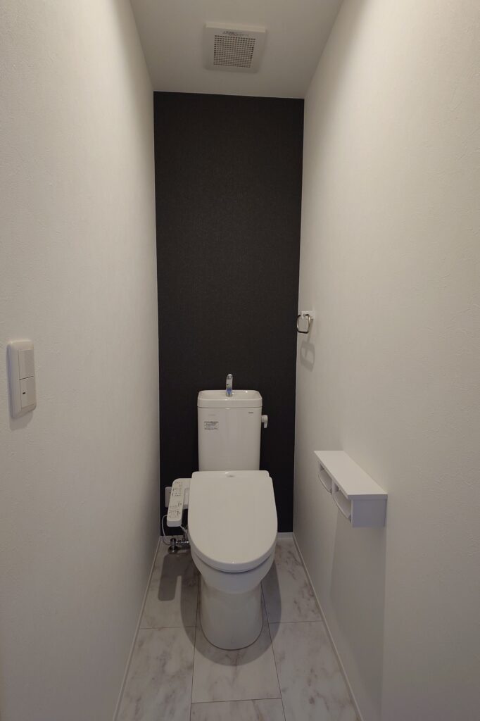金沢市涌波の戸建賃貸住宅のトイレ内観。ブラックのアクセントクロスを採用し、シンプルで落ち着いたデザインに仕上げた空間。