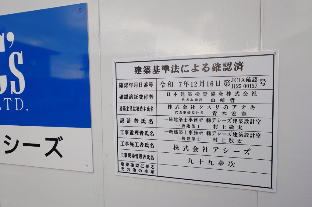 工事現場の看板に記載された株式会社クスリのアオキの名称を写した写真。