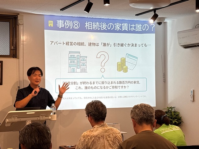 高山不動産のセミナールームにて、高山修一社長がスライド資料の前で立ち、参加者に向けて賃貸経営の具体的なトラブル事例や解決策について熱心に解説している様子。