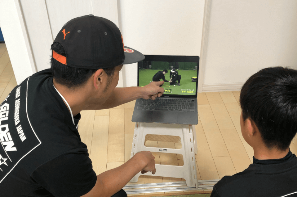 パソコンの野球指導動画を指差しながら、子どもに説明する指導者。