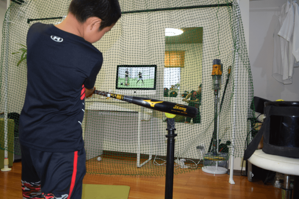 モニタの映像と鏡に映る自分を見ながら、ボールを台に置いて打つ練習をする男の子の姿。