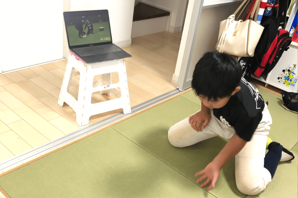 パソコンで動画教材を見ながら室内でキャッチャーのフォーム練習をする男の子の姿。